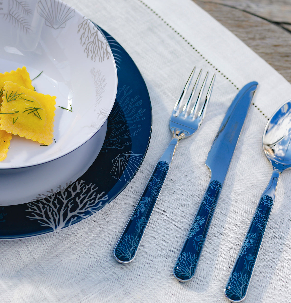 Bestekset Living 24-delig - maritiem blauw met koraal print 18025 Marine Business op een placemat met een stukhe van het Living bootservies