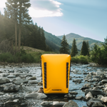 Dometic PSC22BP koelrugzak – waterdichte koeltas backpack 22L in kleur Glow staand in de natuur in een beekje omringt met water en bomen