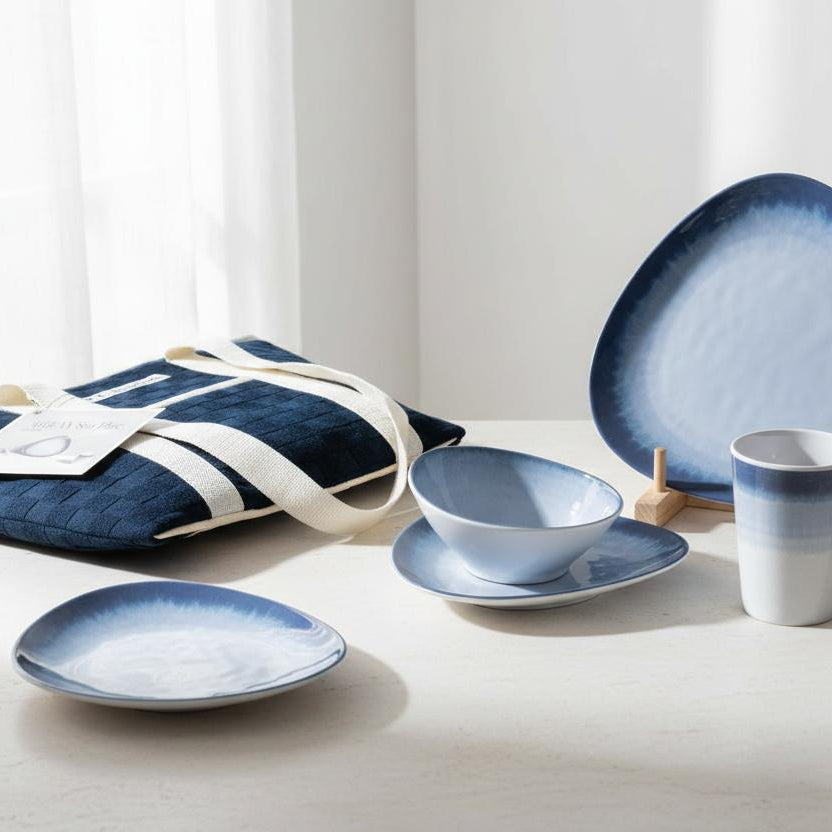FF Collection Aegean Sea Blue 16-delige melamine servies set anti-slip met uitgestald op een witte tafel met de koeltas er liggend naast en witte gordijnen op de achtergrond