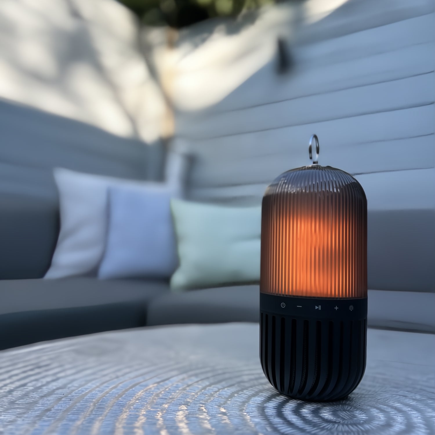 Flamefield Flamelamp in de tuin op een aluminium bijzettafel met een bank met kussens op de achtergrond