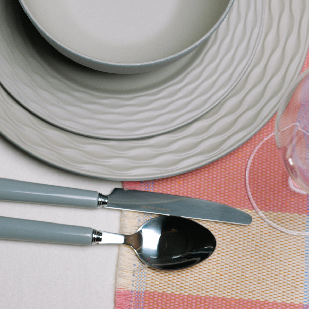 Flamefield Ripple Sand RS0112 melamine servies zand, grijs, natuur relief met bestek op gekleurde placemat ingezoomd