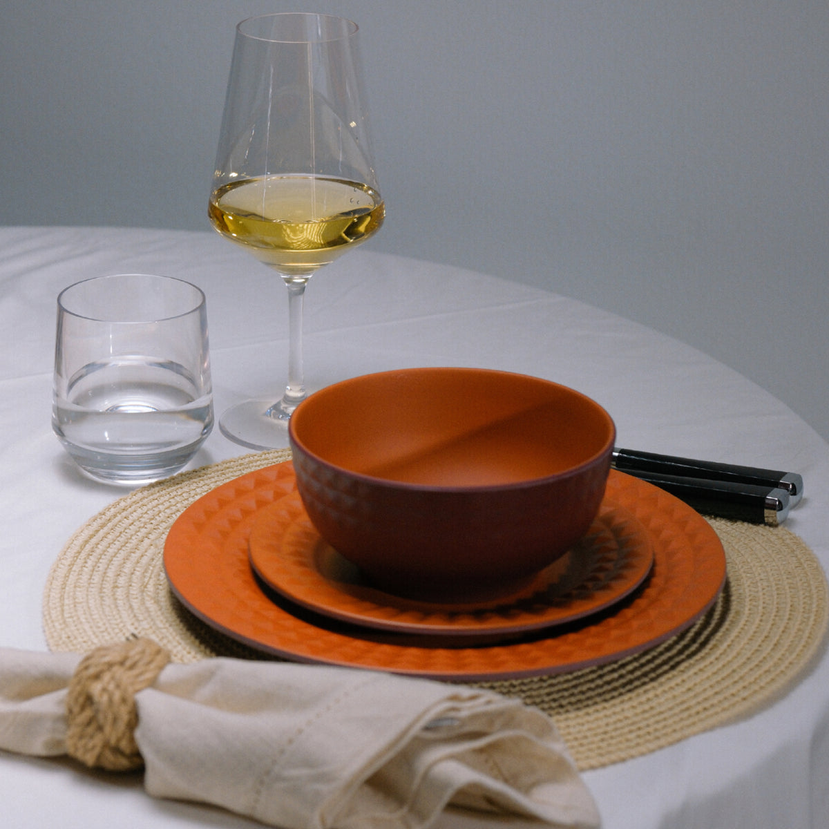 Flamefield Viva Terra melamine servies bordeaux, rood met reliefrand dinerbord, ontbijtbord, kom, op tafel met witte wijnglas en waterglas op placemat 