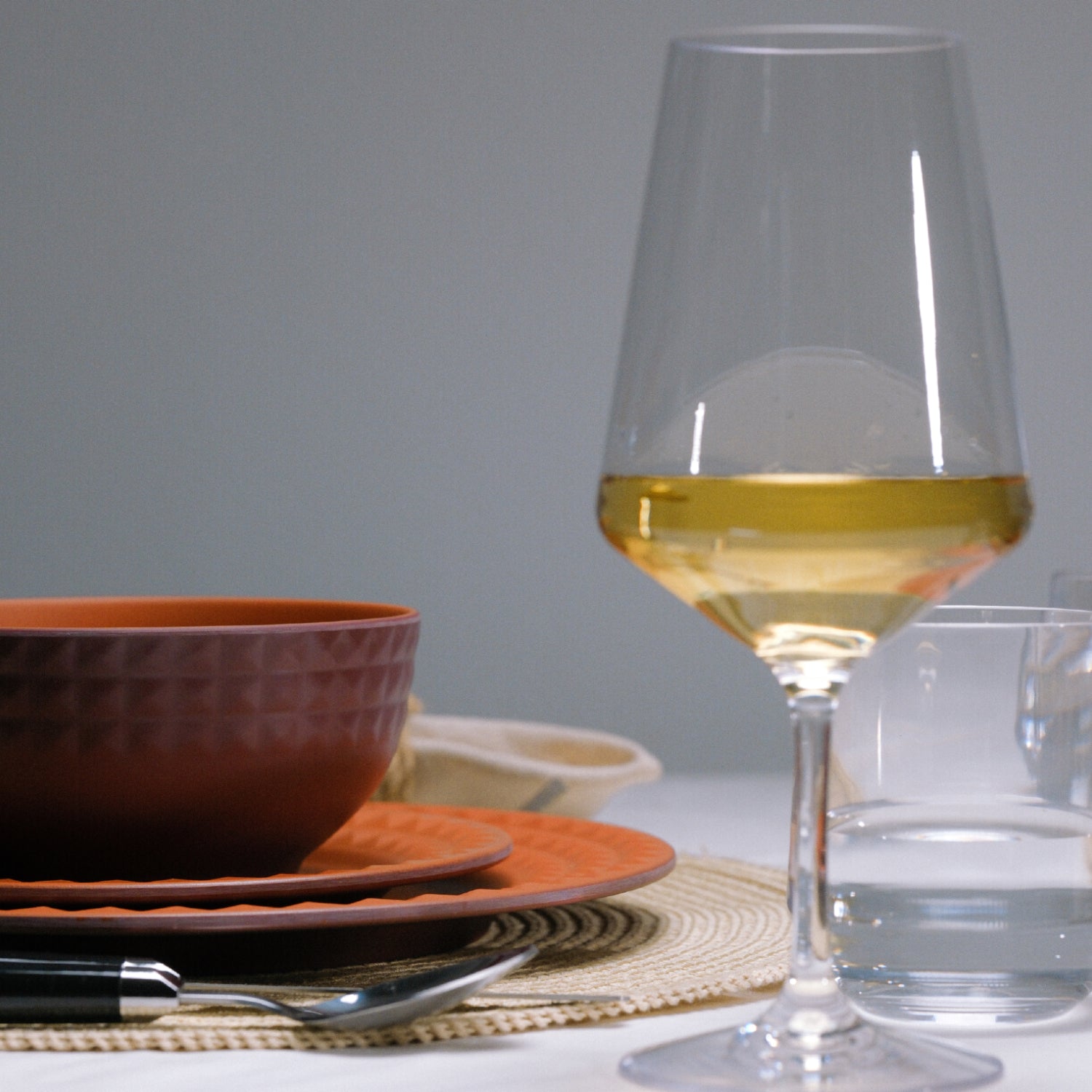 Flamefield Viva Terra melamine servies bordeaux, rood met reliefrand dinerbord, ontbijtbord, kom, op tafel met  zwart bestek en glas wijn met witte wijn gevuld