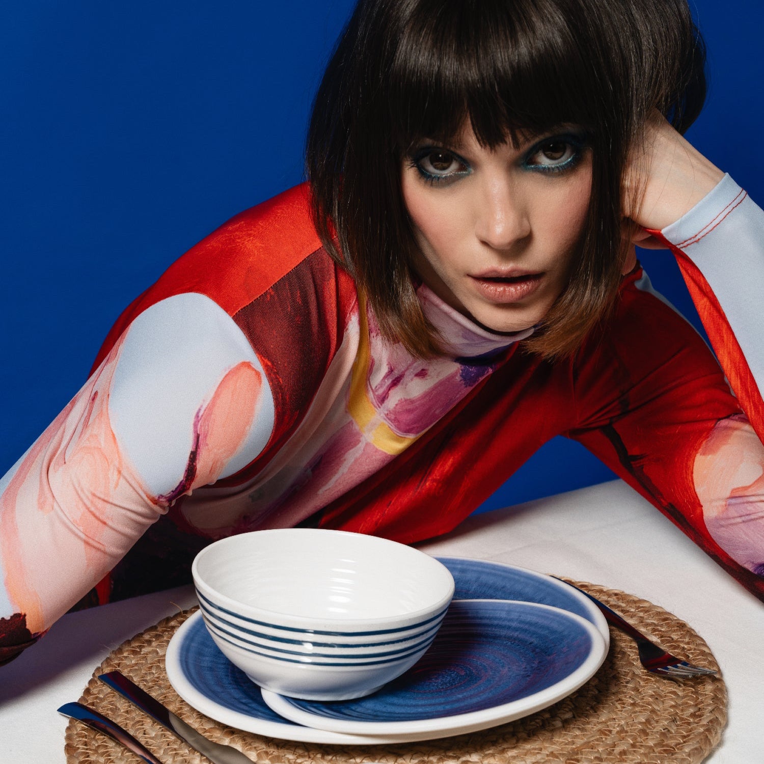 Flamefield sfeerbeeld van fotomodel met kort bruin haar en strakke pony, Flamefield  onbreekbaar servies Azure blauw met wit AZ0112 op een rieten placemate met een witte mok en bestek