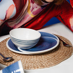 Flamefield sfeerbeeld van fotomodel met kort bruin haar en strakke pony, Flamefield  onbreekbaar servies Azure blauw met wit AZ0112 op een rieten placemate met een witte mok en bestek ingezoomd