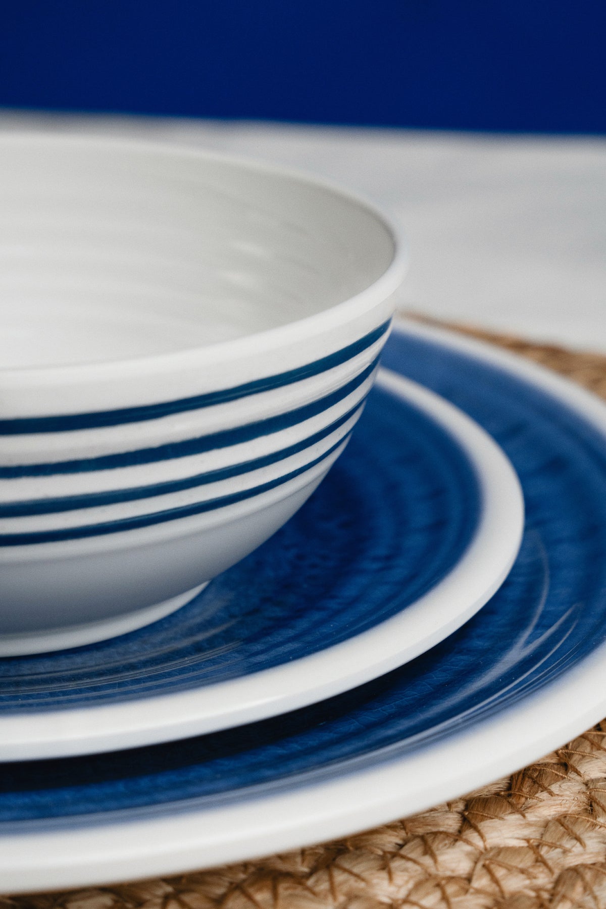 Flamefield sfeerbeeld van onbreekbaar servies Azure blauw met wit AZ0112 op een rieten placemat ingezoomd als een lijnenspel vooraanzicht