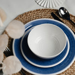 Flamefield sfeerbeeld van onbreekbaar servies Azure blauw met wit AZ0112 op een rieten placemat ingezoomd met een vork mes en lepel van roestvrijstaal