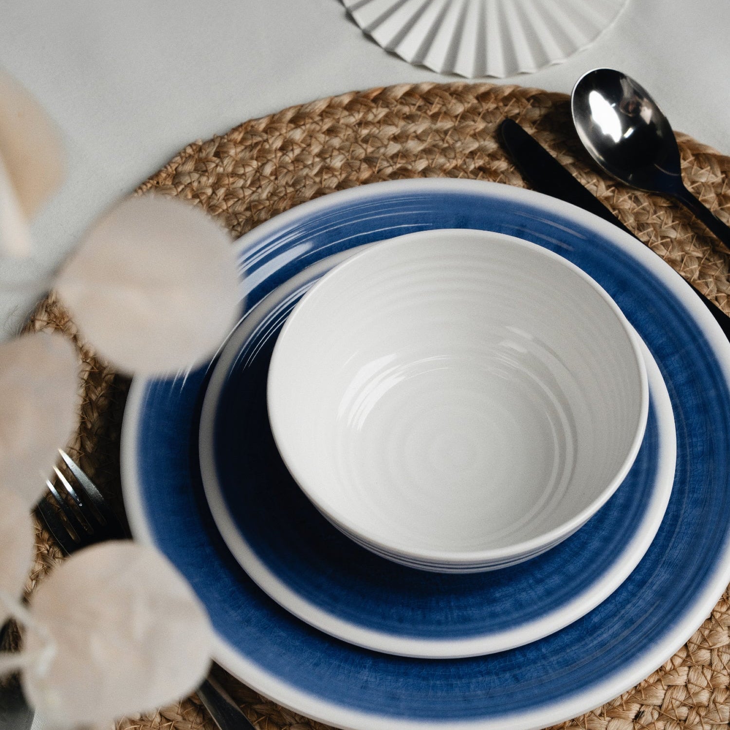 Flamefield sfeerbeeld van onbreekbaar servies Azure blauw met wit AZ0112 op een rieten placemat ingezoomd met een vork mes en lepel van roestvrijstaal