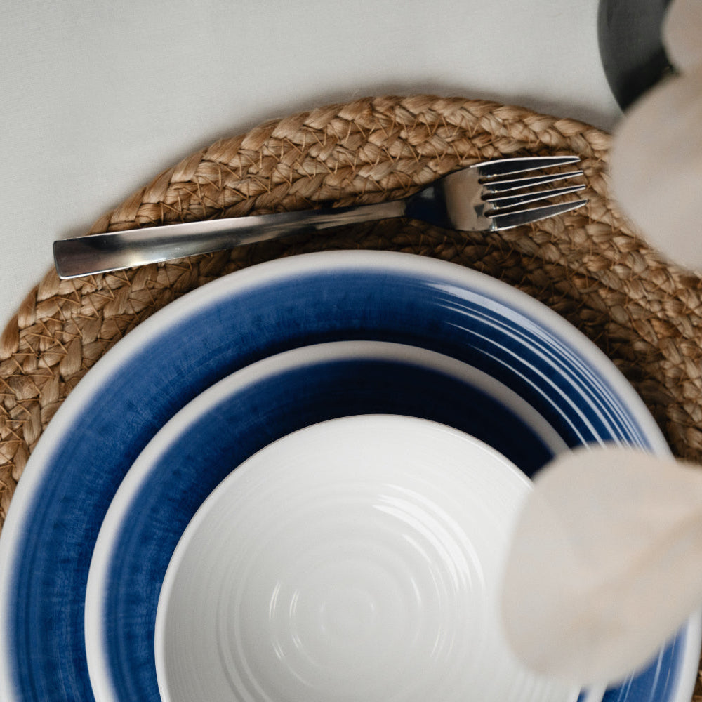 Flamefield sfeerbeeld van onbreekbaar servies Azure blauw met wit AZ0112 op een rieten placemat ingezoomd met een vork van roestvrijstaal