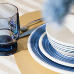Flamefield sfeerbeeld van onbreekbaar servies Azure blauw met wit AZ0112 op een rieten placemat met een witte mok en bestek  met blauwe wijnglas Heavy Base ingezoomd