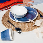 Flamefield sfeerbeeld van onbreekbaar servies Azure blauw met wit AZ0112 op een rieten placemate met een witte mok en bestek  op een placemate van riet