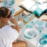 Harmony Mare Blue melamine servies - wit met koraaldecoratie en parelrand samen met aqua onbreekbaar glaswerk en bootkussens van Marine Business met vrouw in sfeerzetting op een boot