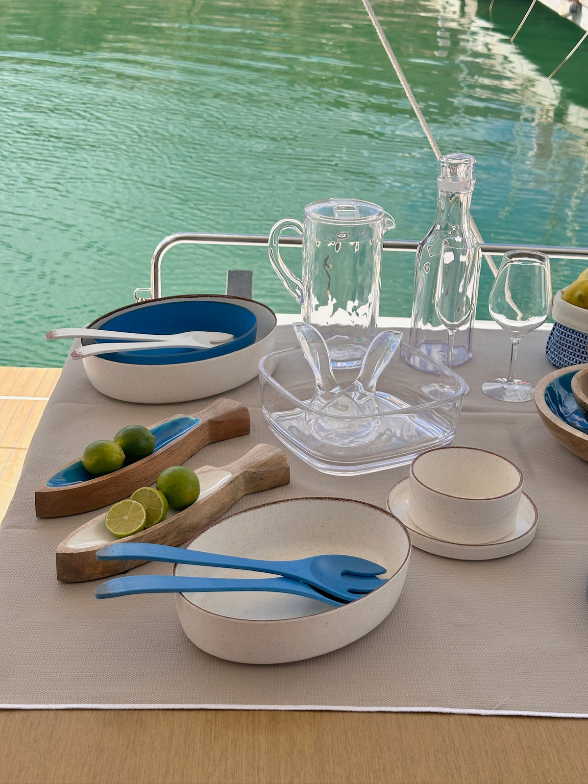 Maldivas bootservies Ivory – modern, zachte creme en onbreekbaar met opstaande rand gemixt met blauw en transparant servies van Marine Business op tafel met water op de achtergrond