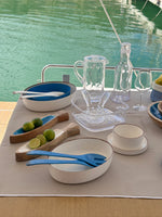 Maldivas bootservies Ivory – modern, zachte creme en onbreekbaar met opstaande rand gemixt met blauw en transparant servies van Marine Business op tafel met water op de achtergrond