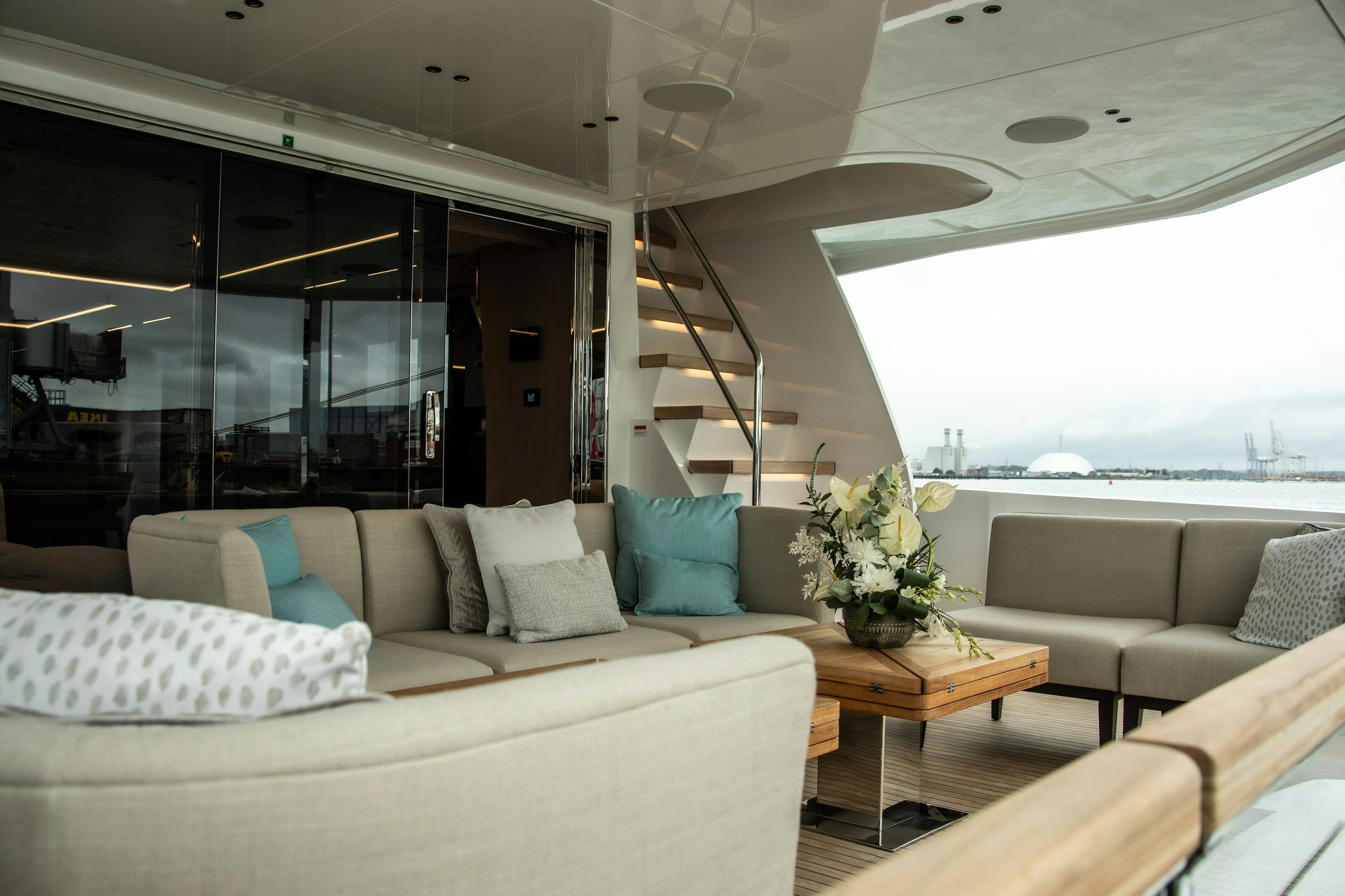 Sfeerbeeld van een superyacht interieur met een beige loungebank en kussens met op de achtergirond een trap met LED verlichting en een glazenwand 