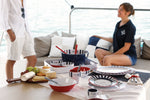 Venezia bootservies - wit met navy gestreept en rode accenten gemixt met accessoires en eten op tafel op een boot met op de achtergrond mensen