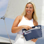 Vrouw met toilettas lachend met een wit shirt met een hand in de toilettas op een zeilboot