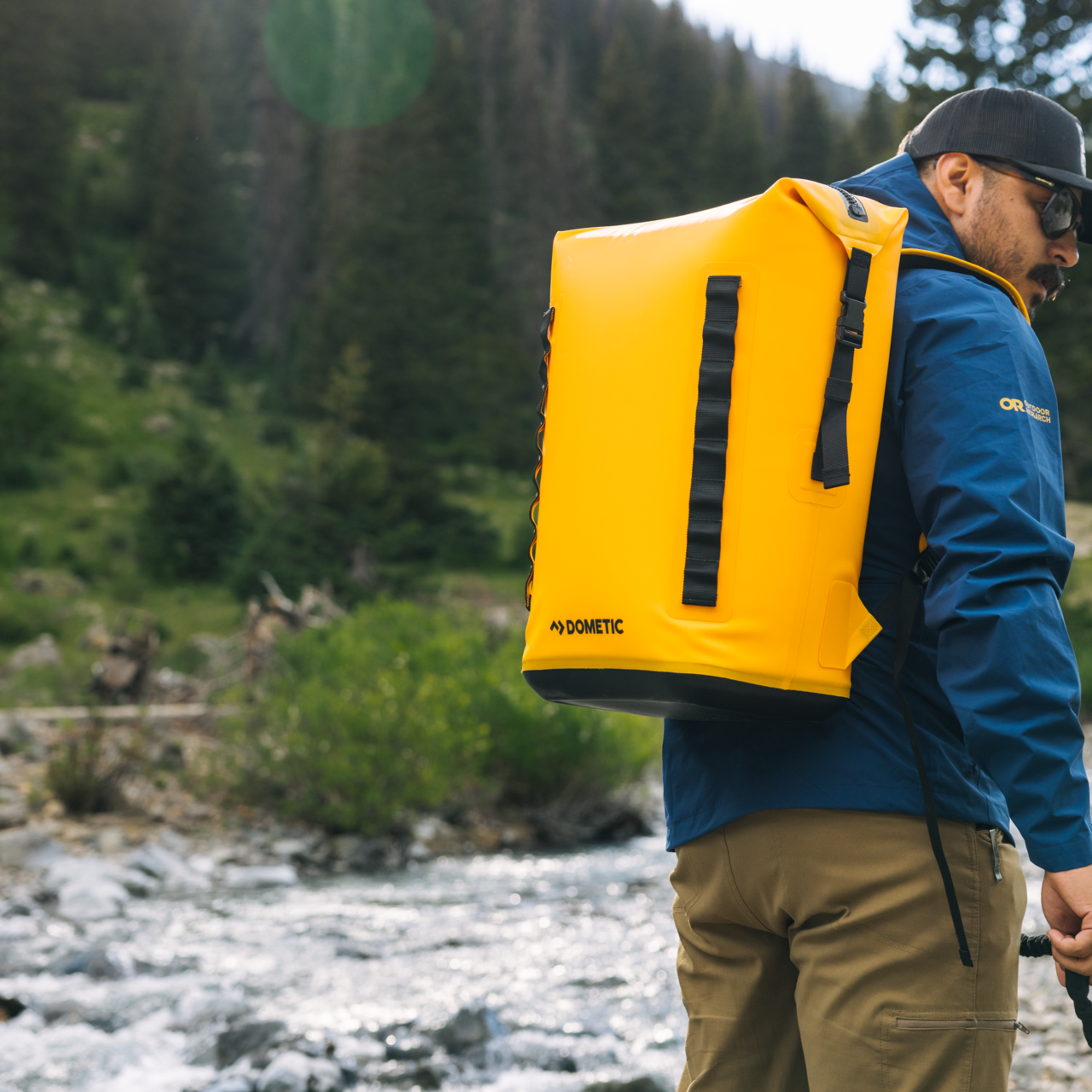 Dometic PSC22BP koelrugzak – waterdichte koeltas backpack 22L in kleur Glow van de achterzijde met comfortabele schouderbanden op de rug van een wandelaar aan het water